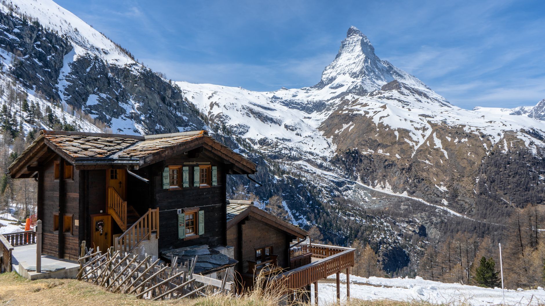 A wooden cabin nestled against towering snow-covered peaks